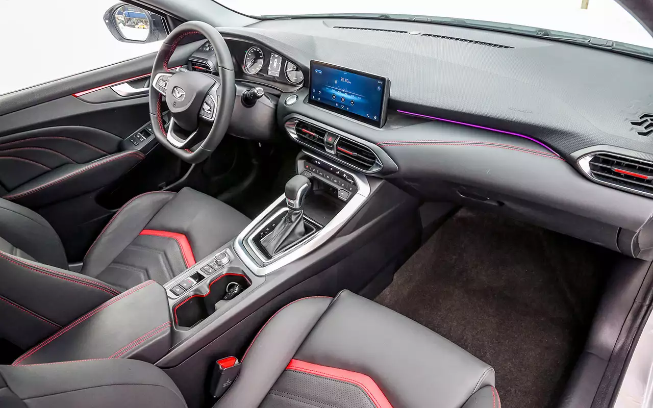 Вариатор 9‑CVT – с возможностью ручного выбора девяти квазипередач. Подрулевых лепестков нет. Перед селектором – площадка беспроводной зарядки телефона. Развернутая к водителю центральная консоль, скошенный по хорде руль, мягкая на уровне вентиляционных жалюзи отделка с красной прострочкой – неплохо задумано, да и собрано на совесть.
